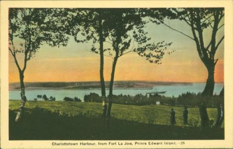 Front of a postcard depicting the Charlottetown harbour. Trees are in the foreground with fields and water in the background. The sky is pink.
