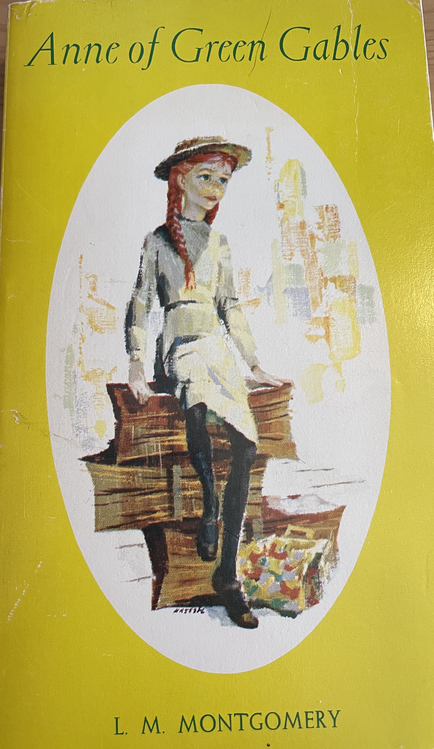 Book cover of Anne of Green Gables. Anne is centred, wearing a white dress and hat sitting on boxes. The background is yellow