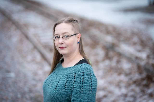 Woman with long light-coloured hair wearing glasses and a green sweater.