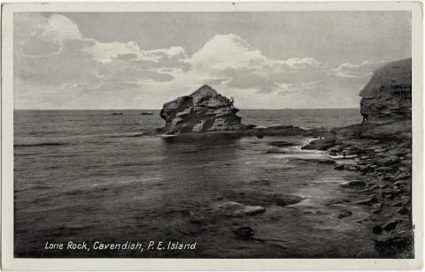 Black-and-white postcard depicting Lone Rock. In the centre of the image is a  rock formation  surrounded by water. On the right is a shore with many smaller rocks.