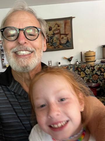 The poet is a smiling man with grey hair and beard and black-framed glasses. His granddaughter is a smiling girl with red hair and freckles.