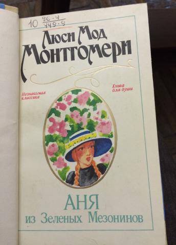 The cover of the first Russian translation of <em>Anne of Green Gables</em> features Anne with red braids, black dress, and a blue-and-white hat with flowers.