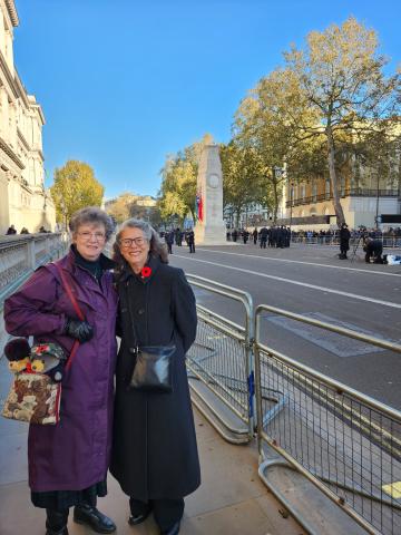 Andrea and her sister Allison Dean stand side-by-side, smiling at the camera, with the Cenotaph in the background Andrea wears a long, grey coat with and Allison wears a long maroon coat.