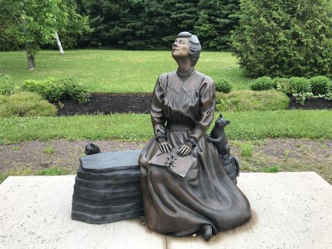 Photo of a bronze statue of L.M. Montgomery sitting on a bench, face upturned, with a book in her lap, and two cats nearby.