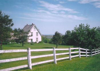 White picket fence along a green field in front of a farm house.