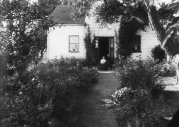Black and white photo of a house with lush gardens.